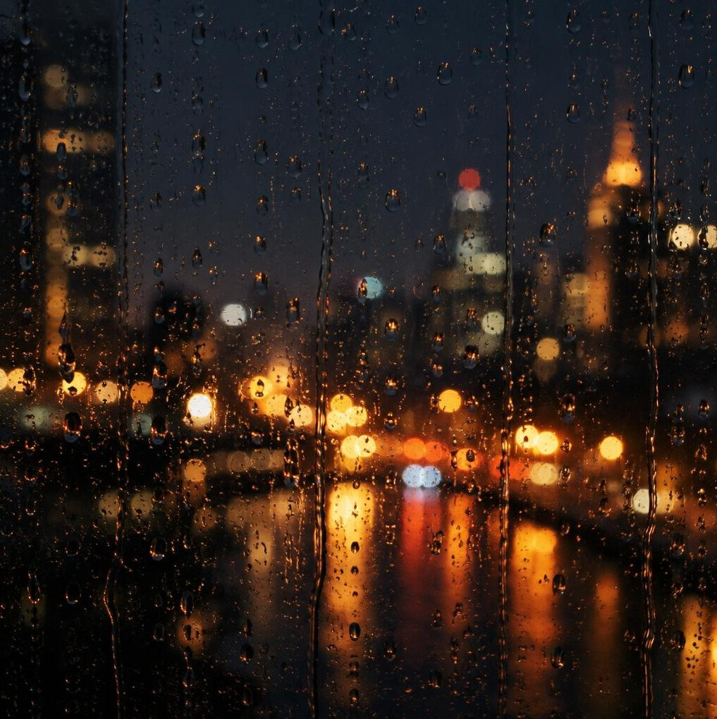 Raindrops on a window with blurred city lights at night